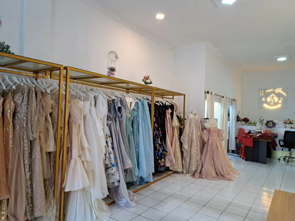 Potret ruangan dalam toko fisik Uptown Gown dengan rak gaun, ruang fitting, dan juga logo neon Uptown Gown